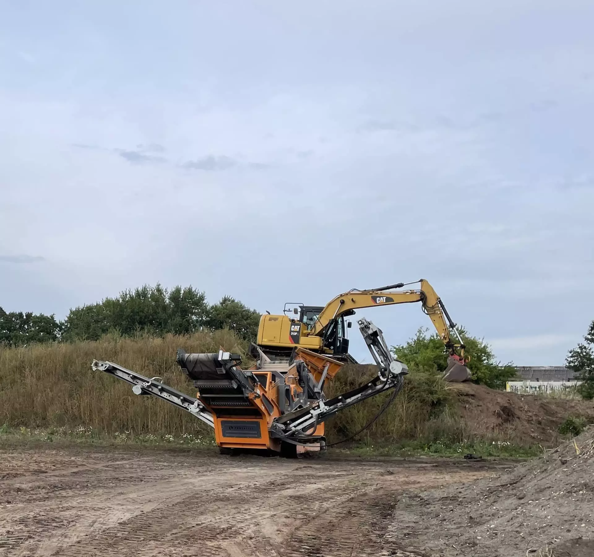 Mobile Siebanlage der Uwe Schröder Erdbau GmbH wird von einem CAT Bagger zur Aufbereitung von Erdmaterial befüllt